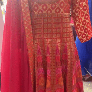 The dress in the image is a vibrant traditional outfit in shades of red, orange, and pink, featuring intricate patterns and embroidery.